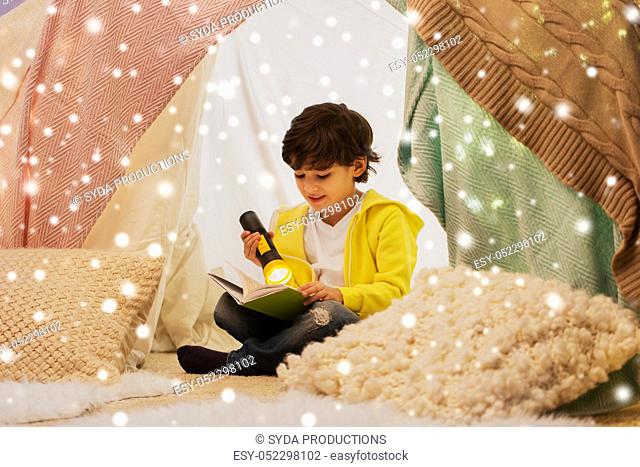 happy boy reading book in kids tent at home