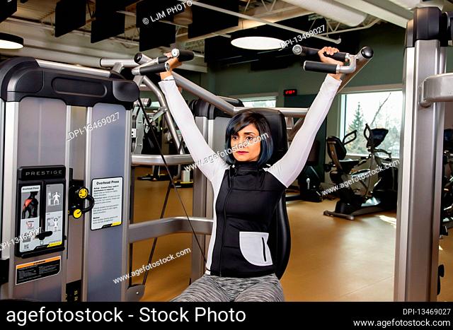 A paraplegic woman working out using an overhead press in a fitness facility; Sherwood Park, Alberta, Canada