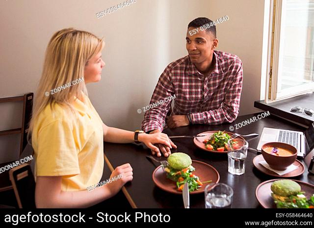 Picture of happy couple spending their free time in vegan restaurant or cafe. People smiling to each other. Date concept