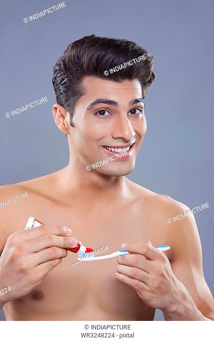 Portrait of young man applying toothpaste on toothbrush