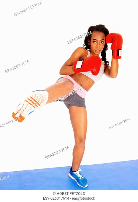 A slim African American girl standing on a blue mat during boxing exercise.with one leg up and red gloves, isolated for white background.
