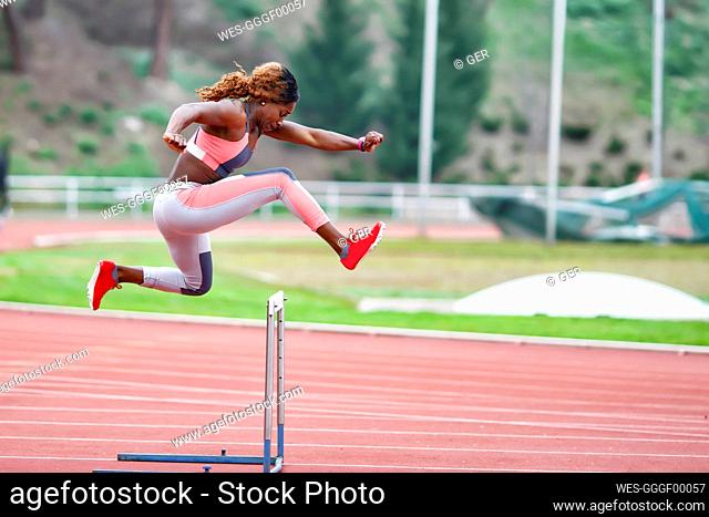 Young sportswoman jumping over hurdle during training