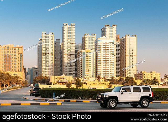 White SUV Car Moving In City Street. New Residential Multi-storey Houses. Cityscape Skyline In Sunny Spring Evening On Blue Sky