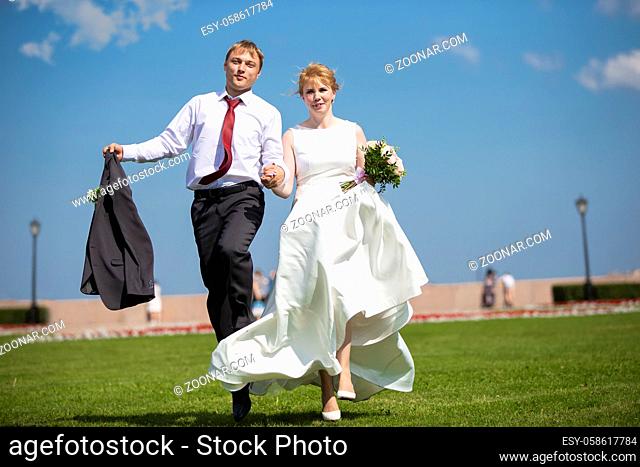 Bride and groom. Beautiful newlyweds run on the grass against the sky