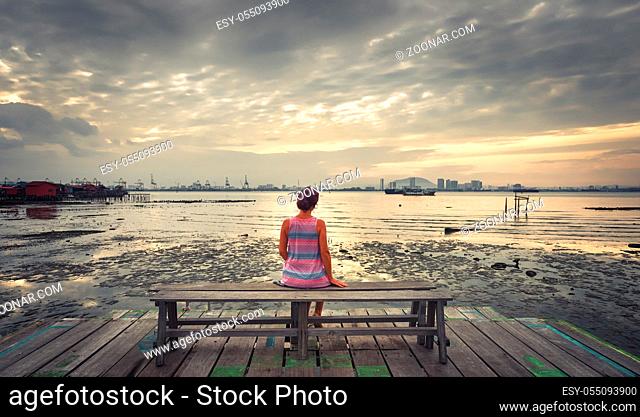 Tourist sitting at Yeoh jetty at sunrise, Georgetown, Penang, Malaysia. Panorama