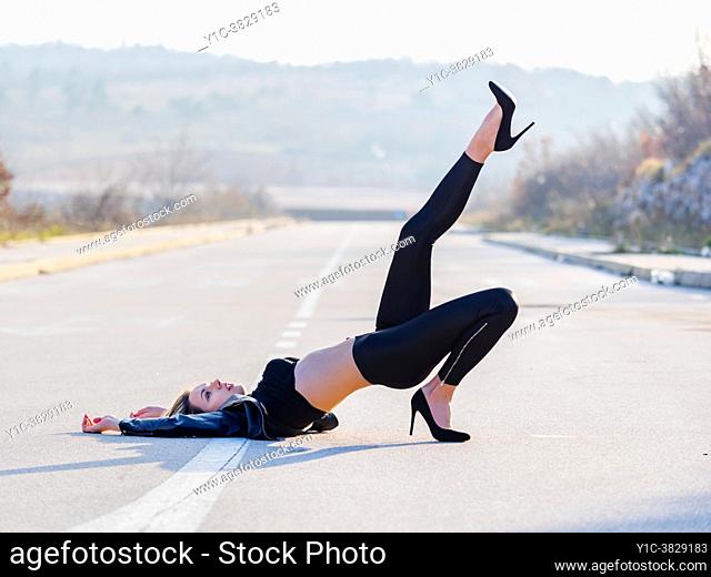 Attractive young woman is raising leg upwards laying on empty road