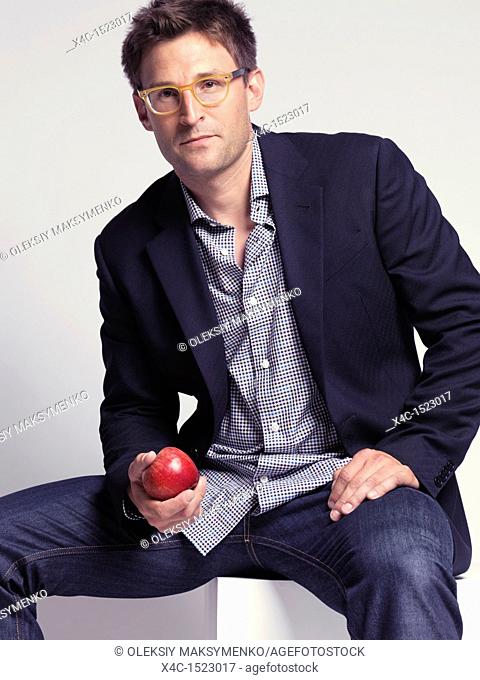 Fashionably dressed man in his thirties wearing jeans and a stylish jacket holding an apple in his hand