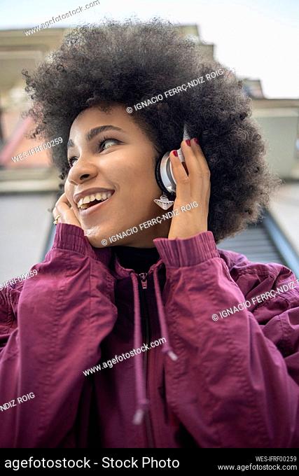 Cheerful woman wearing headphones against built structure