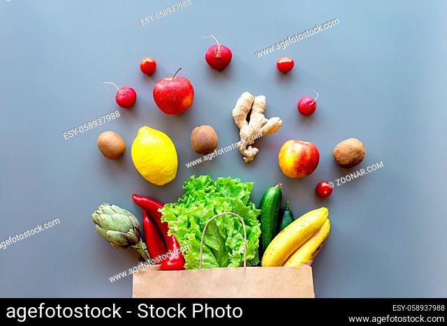 Healthy and organic food flay lay concept on gray background. Eco bag with scattered lettuce salad leaves, apples, kiwi, radish, lemon, cucumber, banana