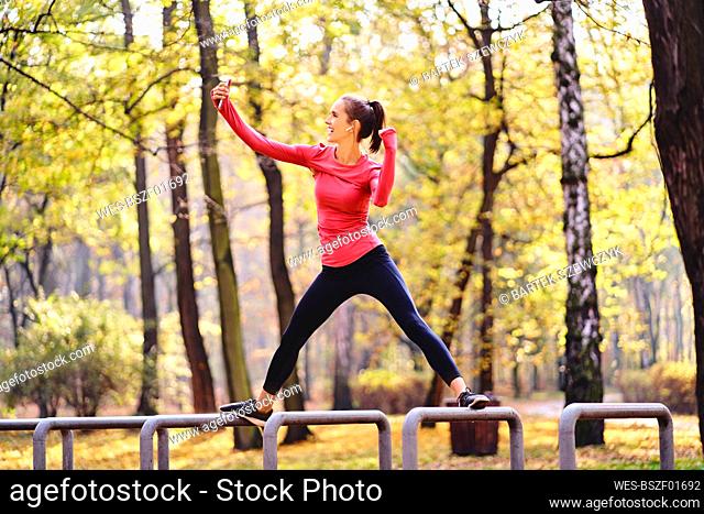 Young female jogger taking a selfie on bicycle stand in autumn forest