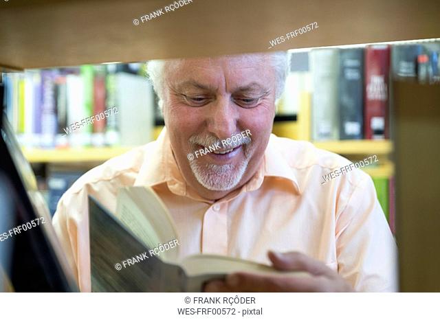 Portrait of smiling senior man in a city library reading book