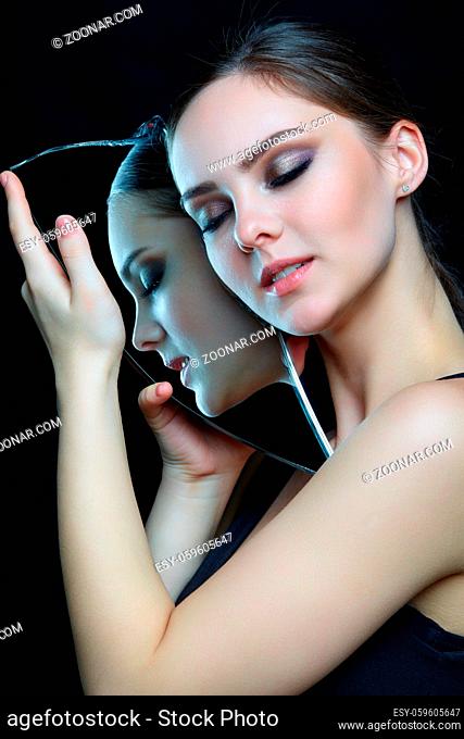Girl with a shard of the mirror. Female with mirror shard in hand posing on gray background. Face reflection in mirror splinter. Eyes closed