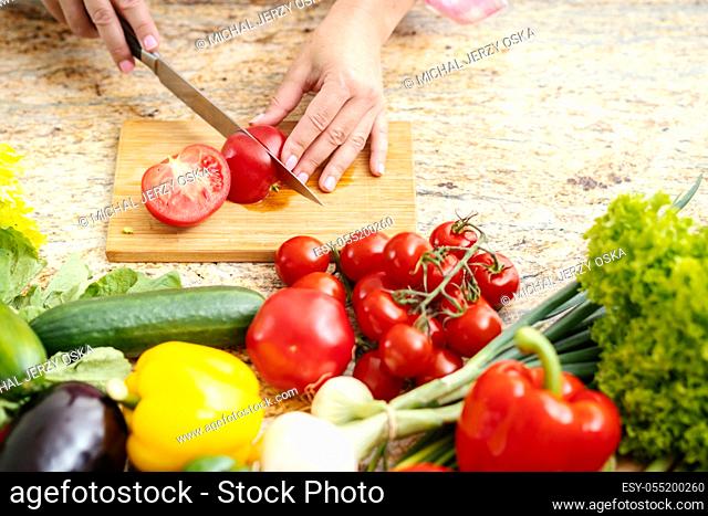 woman's hands are cutting tomatoes on a kitchen table with vegetables