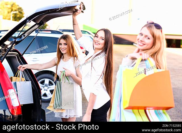 Group of girls after shopping loading a shopping bags in a car trunk