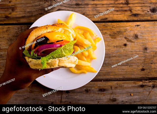 Hands of african american man having burger while french fries in plate, copy space