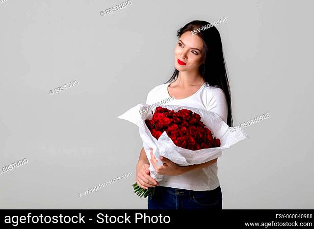 beautiful smiling young woman holding large bouquet of red roses on gray background. flower delivery