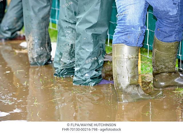 Farmers wearing wellington boots and waterproofs standing in puddle of muddy water, Great Britain, june