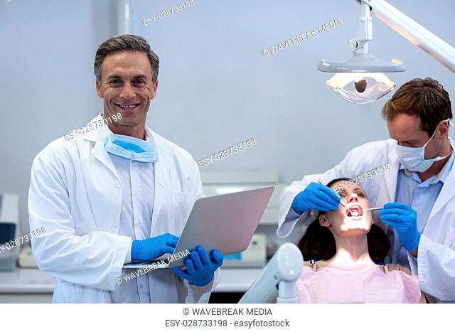 Portrait of dentist holding laptop at dental clinic