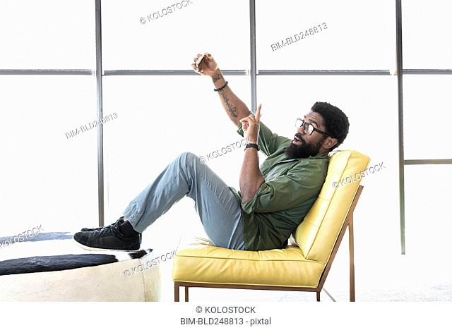 Black man sitting in chair posing for cell phone selfie