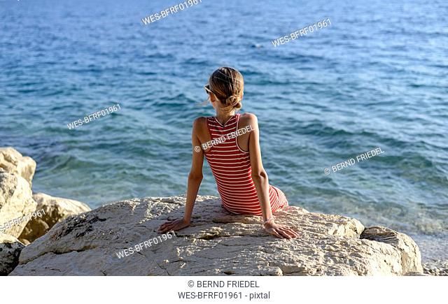 Croatia, Lokva Rogoznica, back view of girl sitting on a rock in front of the sea