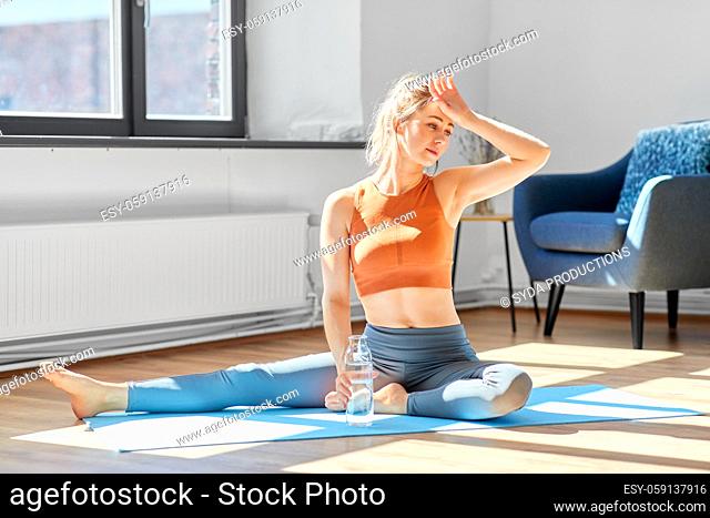 tired woman with water resting on yoga mat at home