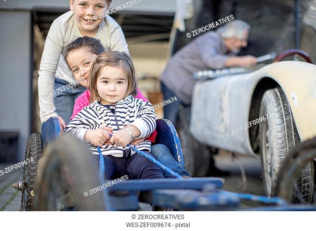Boy pushing two little girls in go-kart