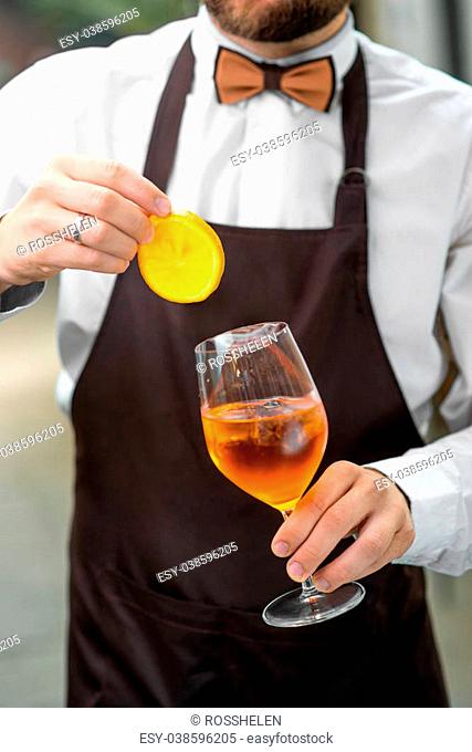 Barman making cocktail with sparkling wine, Aperol and orange. Close up view focused on hands