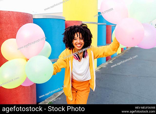 Smiling woman holding colorful balloons in front of pipes