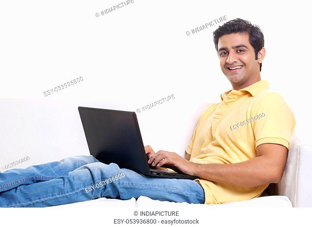 Portrait of handsome young man on sofa using laptop