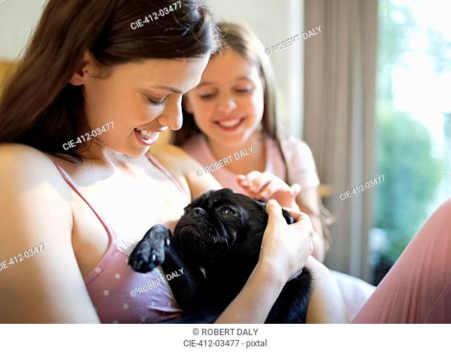 Mother and daughter petting dog in bed