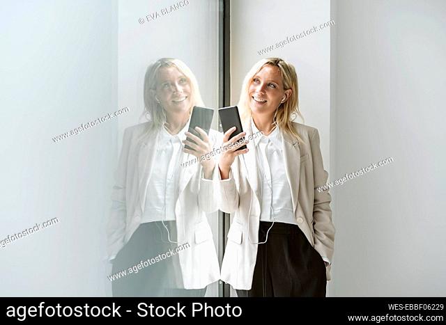 Smiling businesswoman holding mobile phone at glass wall