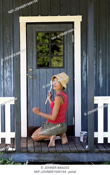 Mature woman painting porch, Sweden