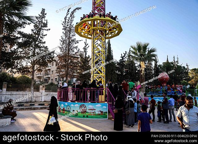 29 June 2023, Syria, Idlib: People ride on the power tower game at the City Park during the celebrations of the Eid al-Adha holiday in Idlib