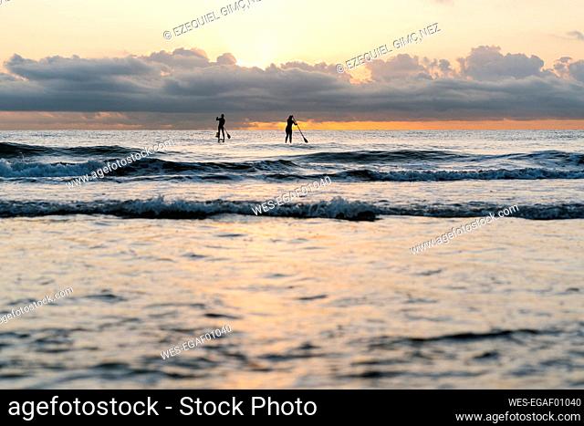 Friends paddleboarding on Mediterranean Sea against sky at dawn