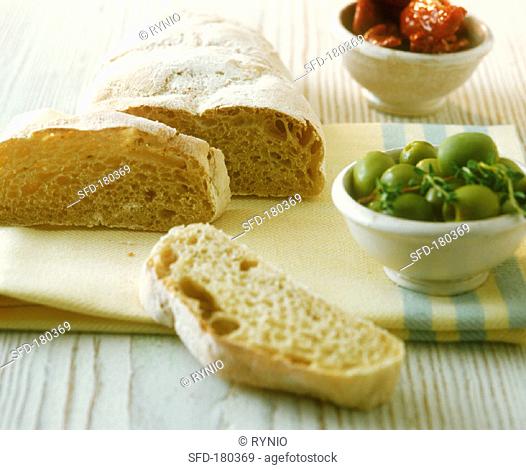 Ciabatta with bowl of green olives on kitchen cloth