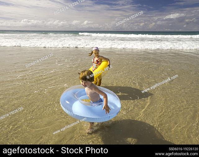 Young children wearing inflatable rings playing in the waves at the beach