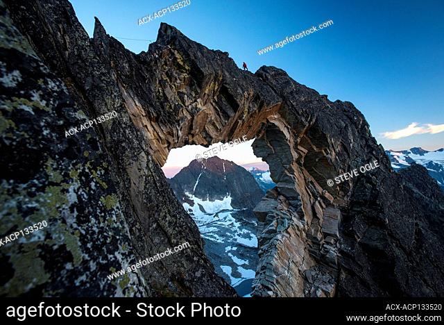 A woman climbs over an impressive natural arch above Jumbo Pass in the Purcell Mountains of British Columbia