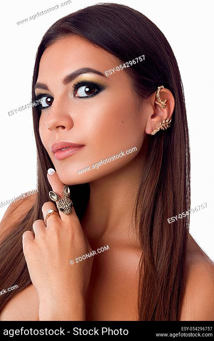Beauty portrait of nude pretty brunette woman with long hair, evening make up, long eyelashes. Female touching face by hand with big ring and looking at camera