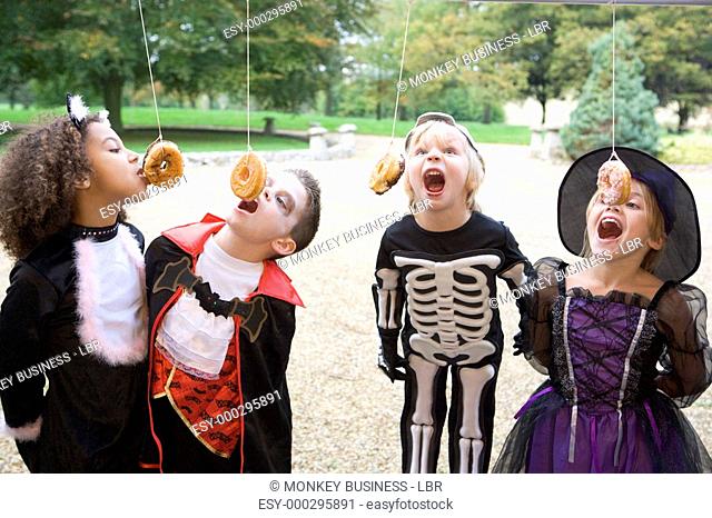 Four young friends on Halloween in costumes eating donuts hanging off strings