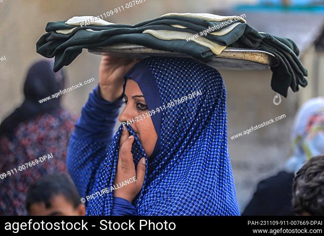 09 November 2023, Palestinian Territories, Khan Yunis: A Palestinian woman carries a tray near a UNRWA school gate. Amid ongoing fighting between Israel and the...