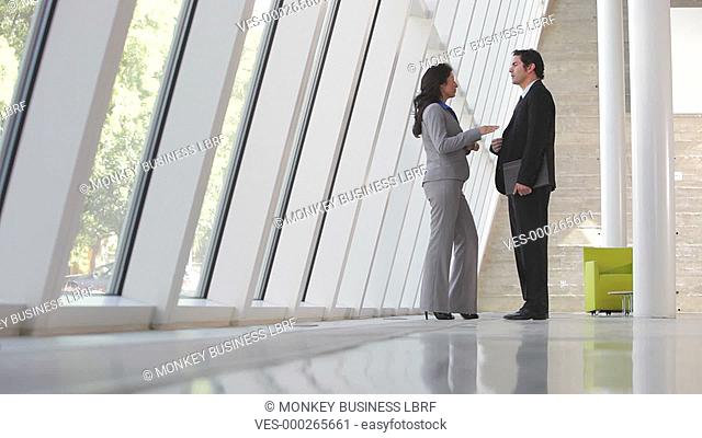 Businessman and businesswoman standing by window in modern office having informal meeting.Shot on Canon 5d Mk2 with a frame rate of 30fps
