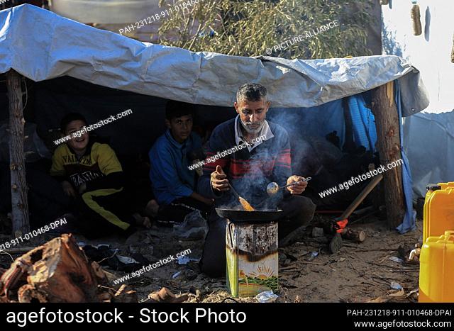 18 December 2023, Palestinian Territories, Rafah: A Palestinian man cooks food in conditions of very limited electricity, water, and food supplies