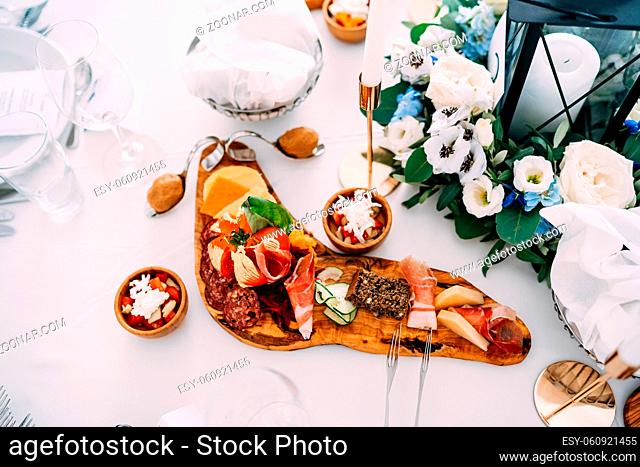 Cutting board with sliced prosciutto, sausage and cheese on the table with bowls of salad and a bouquet of flowers. High quality photo