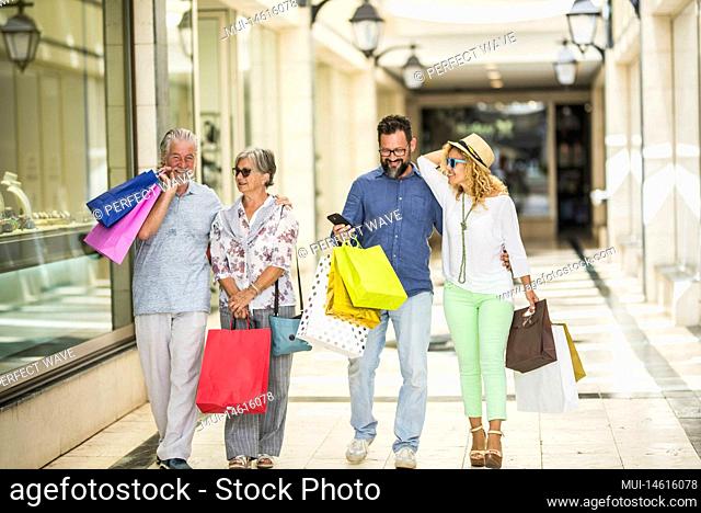 group of four people of adults and seniors doing shipping together in a mall with a lot of shopping bags - man looking at his phone