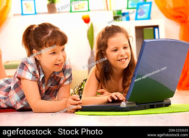 Elementary age girls having fun together at home using laptop computer, browsing internet