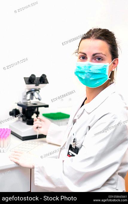 Cheerful female scientist with protective mask posing at the laboratory