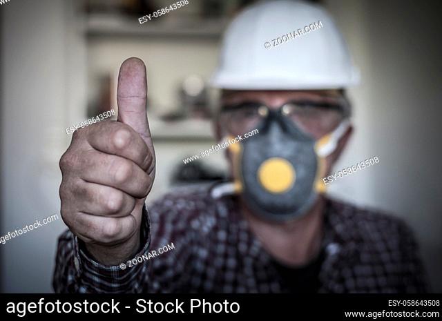 Arbeiter zeigt Daumen hoch, mit Schutzhelm, Schutzbrille und Schutzmaske, geringe Tiefenschaerfe