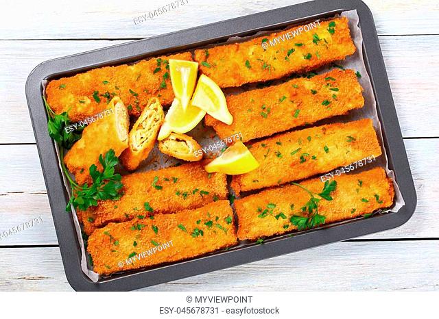delicious Crispy breaded taquitos stuffed with Chicken and grated cheese with lemon slices and parsley in baking dish on wooden table, view from above