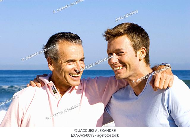 Senior man and adult son hugging at beach