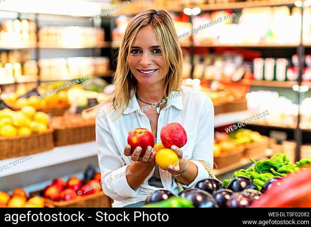 Woman holding apples and lemons while shopping at supermarket